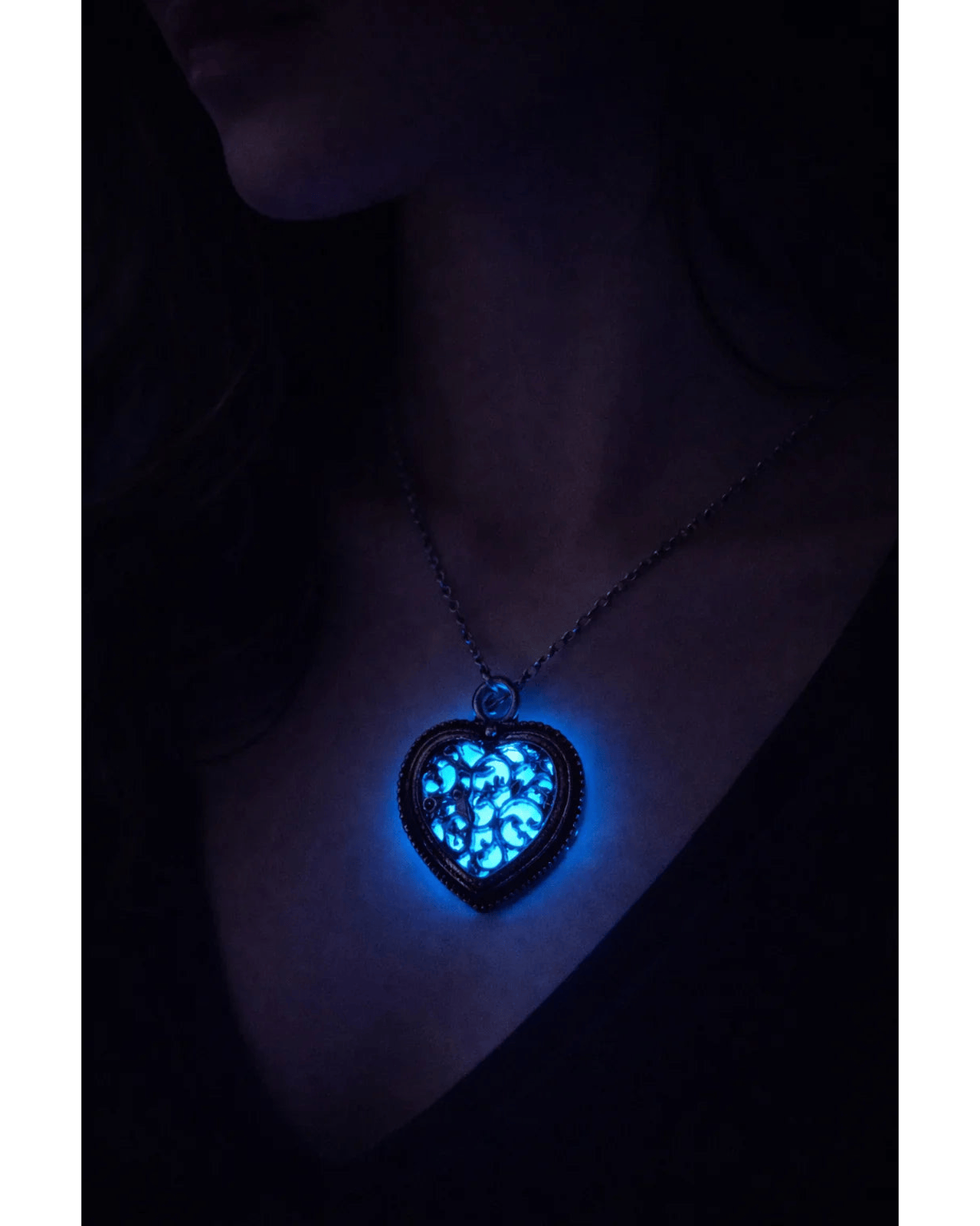 Antikt filigranhjärta med blått sken buren på person i mörker