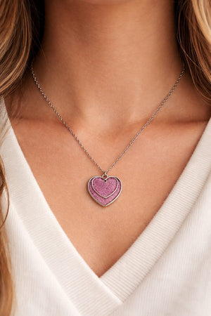 Dubbelt hjärthalsband med rosa glitter buren på person i dagsljus