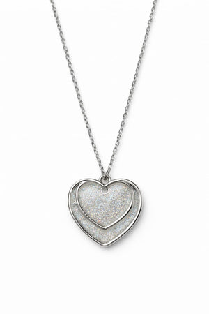 Dubbelt hjärthalsband med silverglitter på vit bakgrund i dagsljus