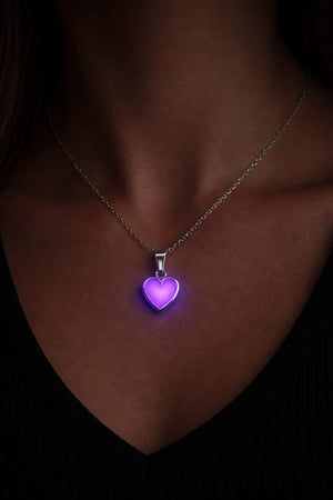 Silverhalsband med rosa hjärta som lyser i mörker på person