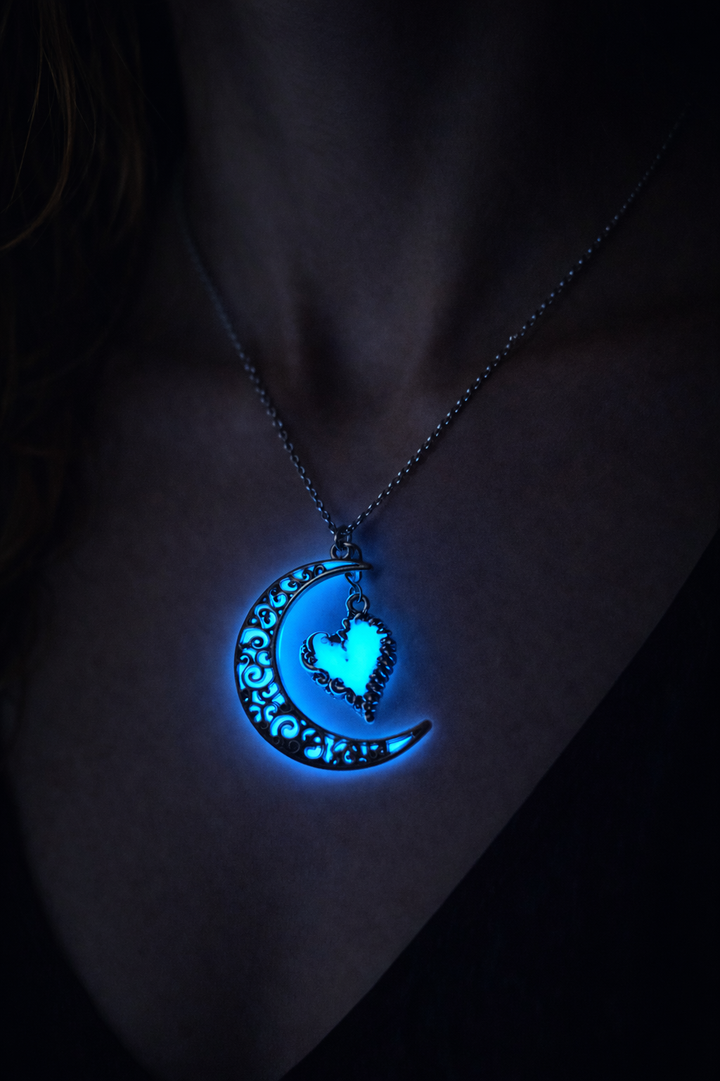 Halvmåne och hjärta halsband med blått sken buren på person i mörker