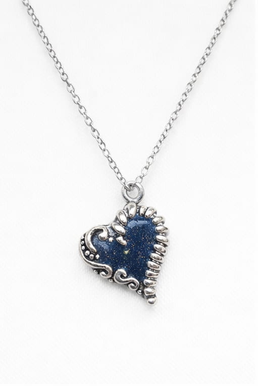 Antikt silverhalsband med mörkblått hjärta och guldkorn i dagsljus
