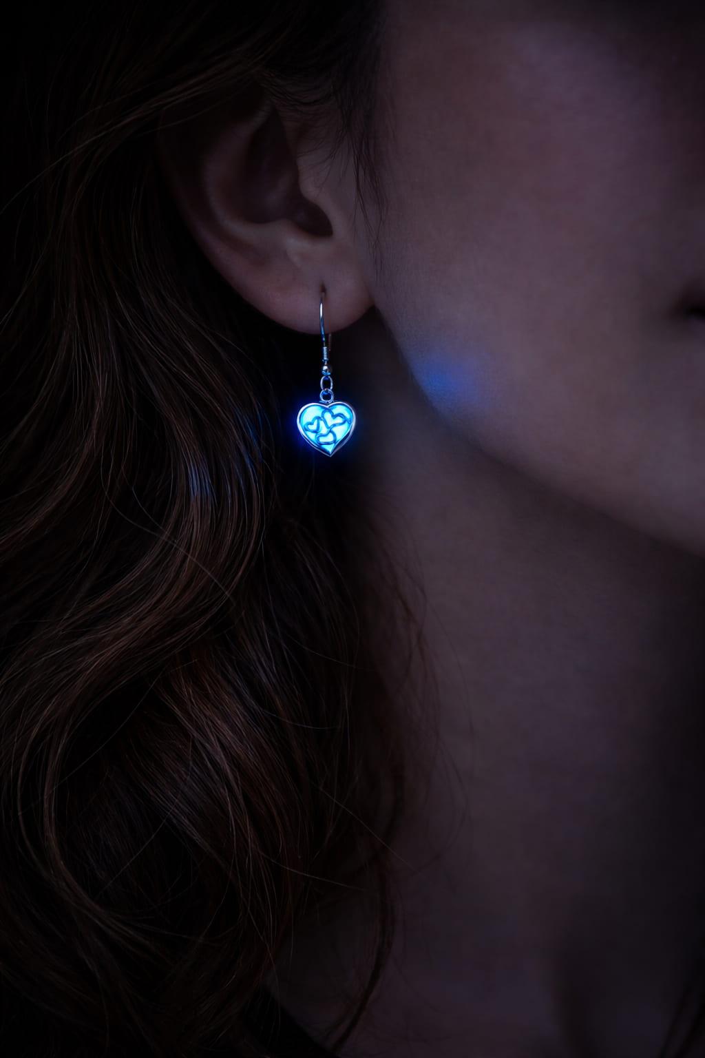 Små självlysande hjärtörhängen med blått sken buren på person i mörker